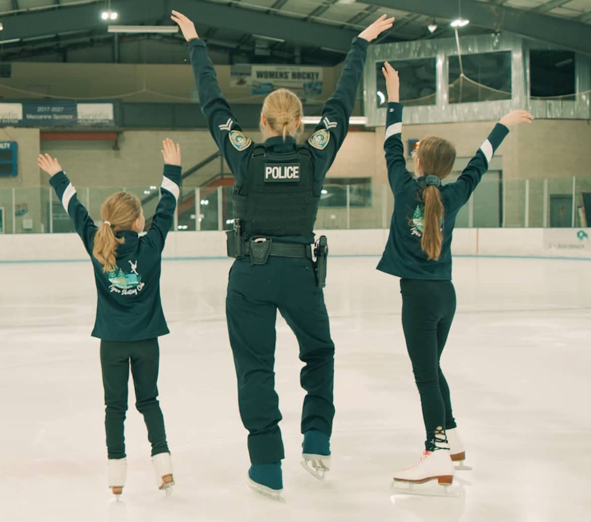 Dressed in her police uniform, Stephanie Kazior leads a couple of young girls on the ice, backs turned.